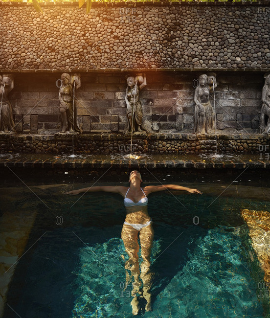 Pacific Islander woman floating in ornate pool