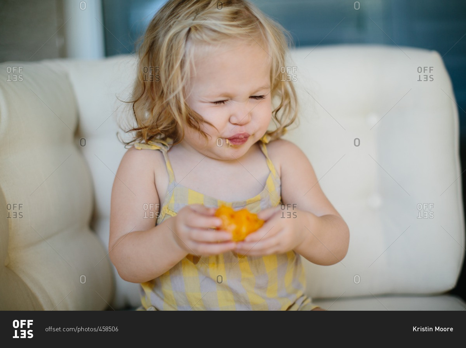Toddler girl making a sour face while eating an orange