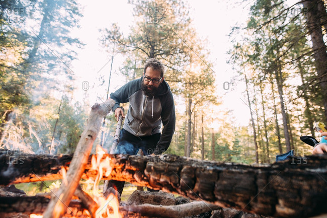 Man stoking campfire with branch