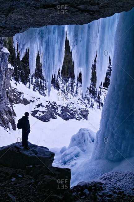 Hiker dwarfed by giant icicles, behind Panther Falls in Winter,  Banff National Park, Alberta, Canada