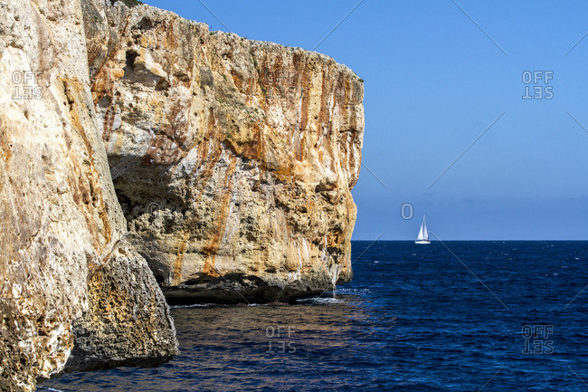 Stone sea cliffs and a sailboat in the distance