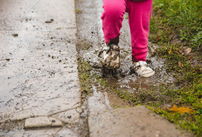 Child in white shoes walking through muddy puddle