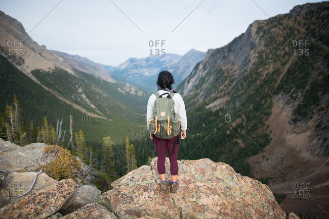 Person standing on a rocky outcrop and looking off into the distance at a scenic overlook in the mountains