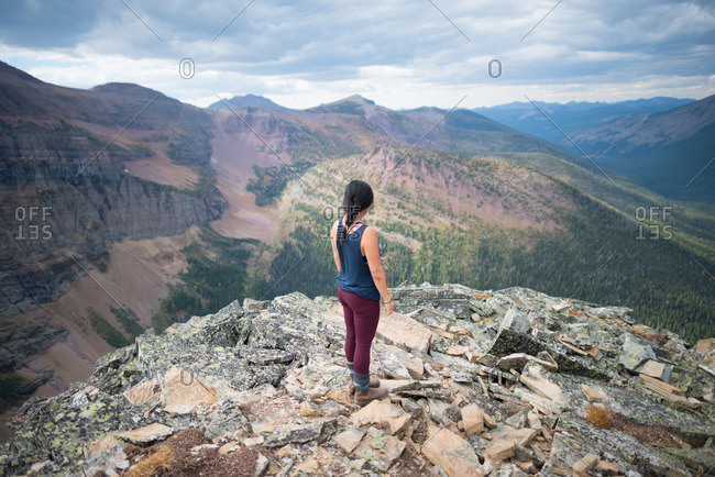 Person standing on a rocky outcrop and looking off into the distance at mountain scenery