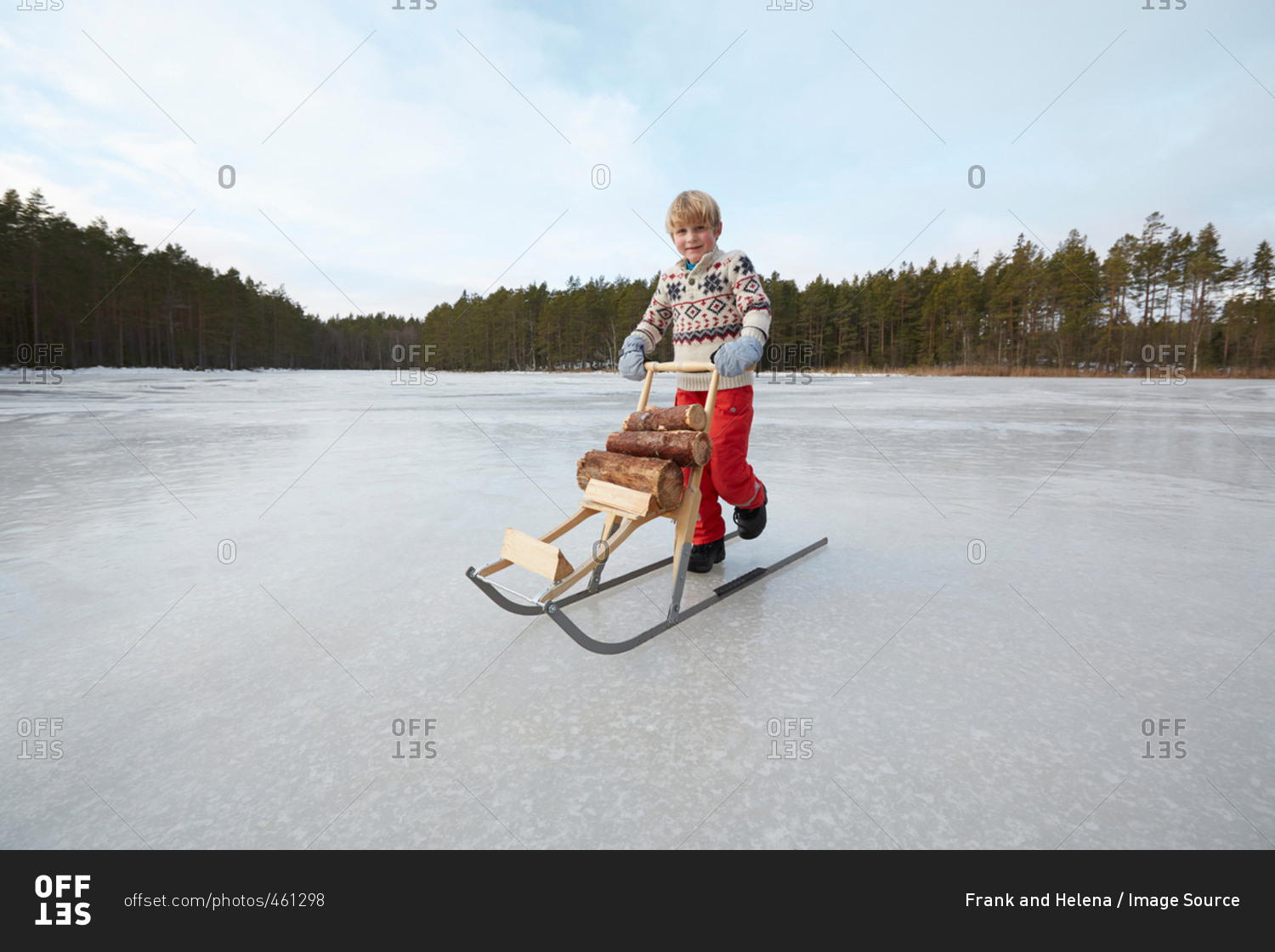 Boy pushing logs on kicksled across frozen lake, Gavle, Sweden