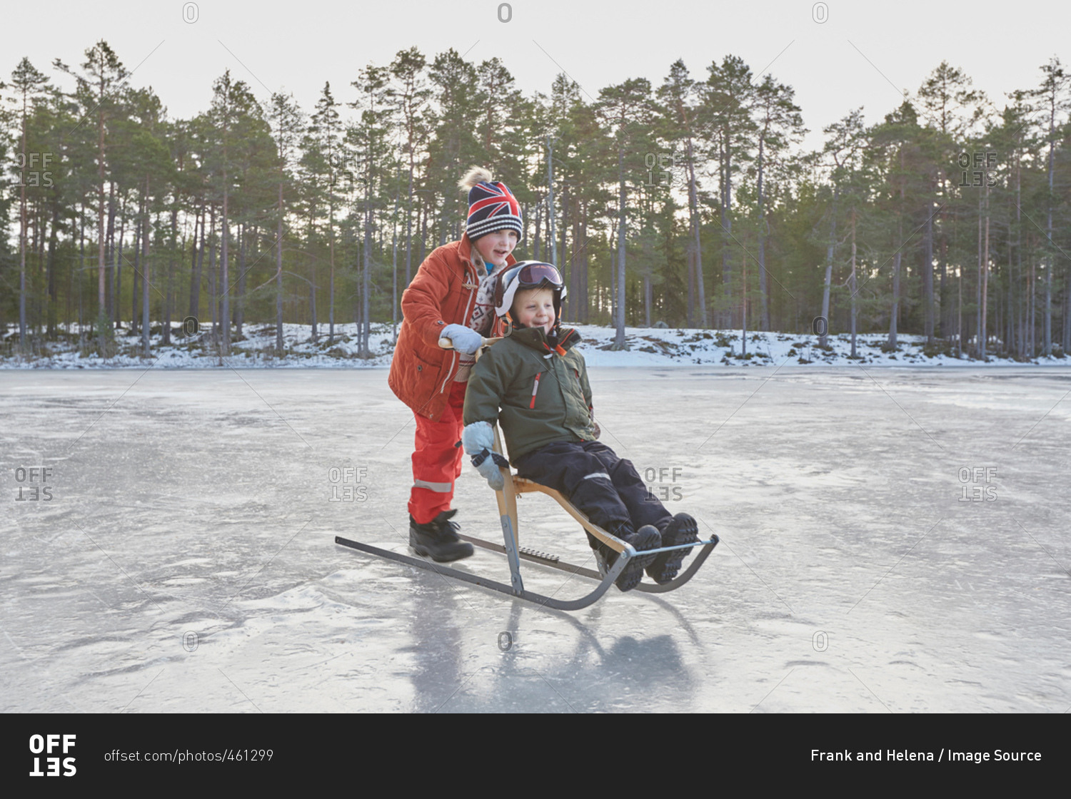 Boy pushing friend on kicksled across frozen lake, Gavle, Sweden