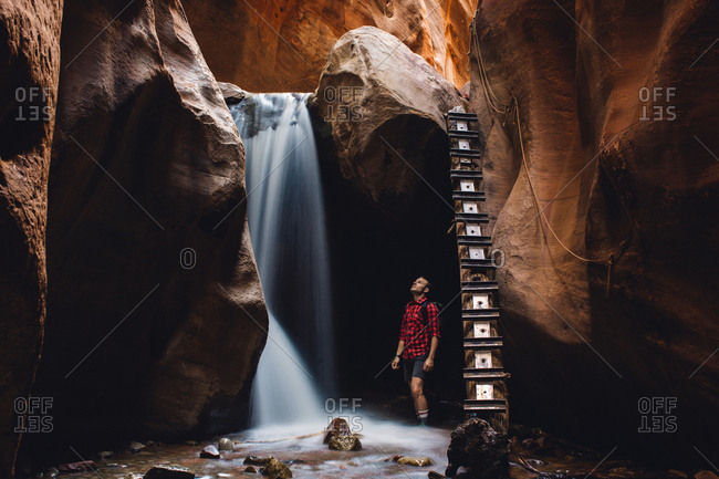 Male hiker looking up at waterfall in cave, Zion National Park, Utah, USA