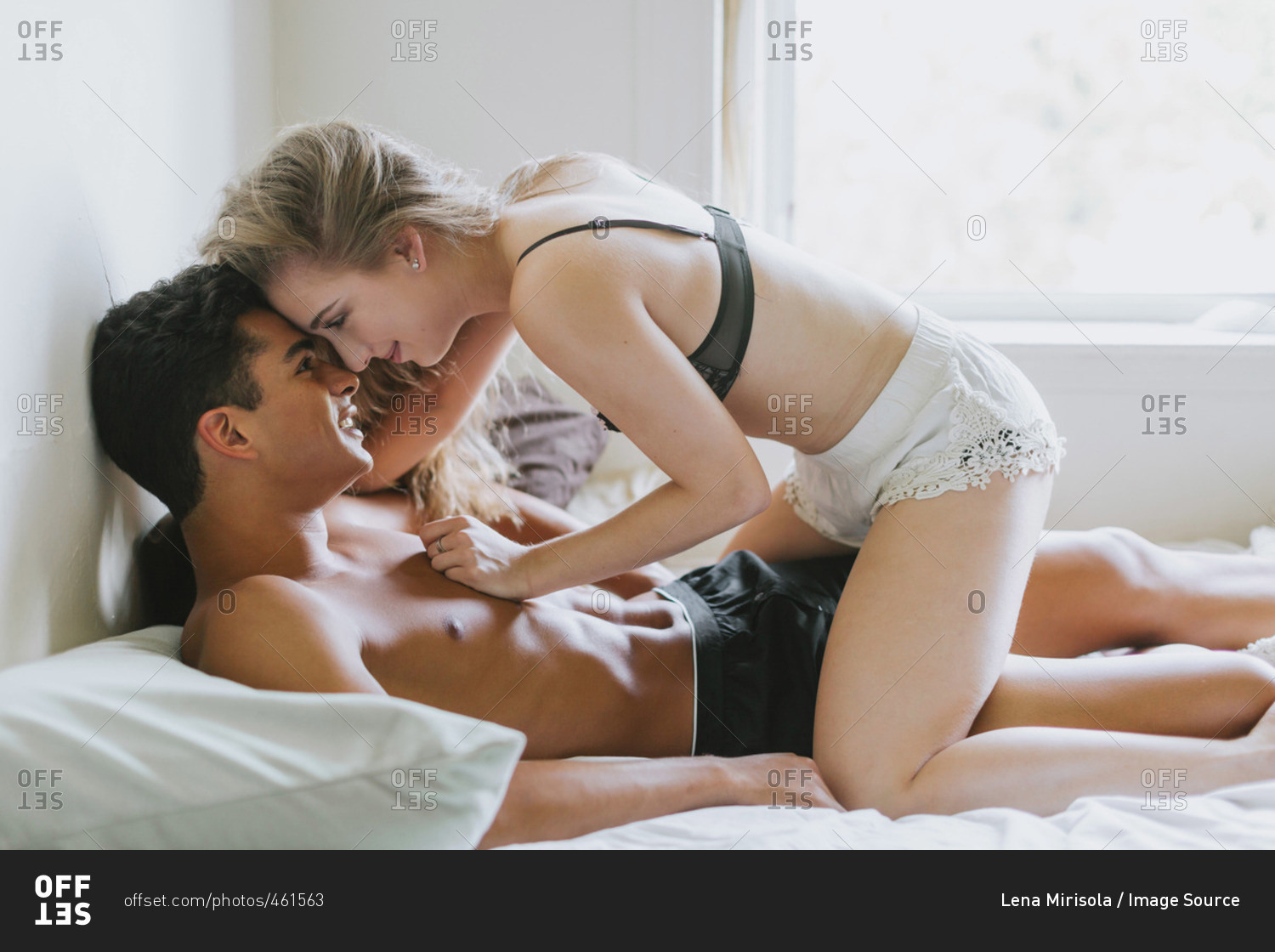 Young woman straddling young man lying on bed. 