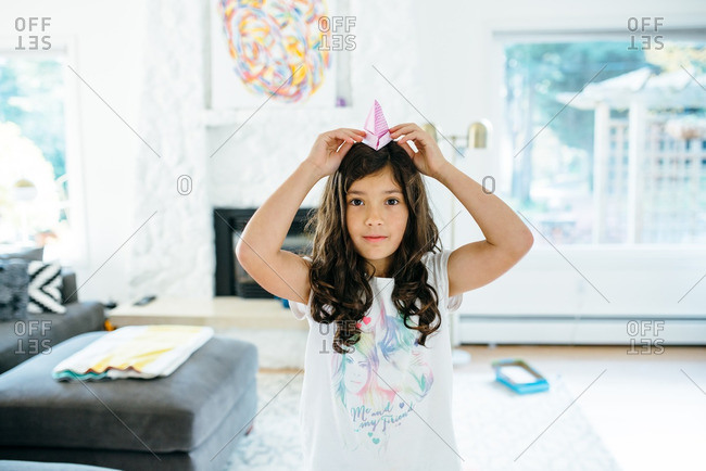 Little girl putting an origami paper hat on her head