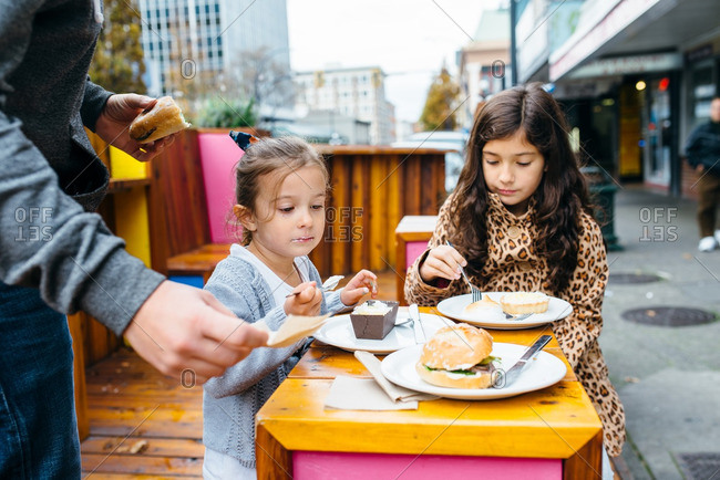Father and two daughters enjoying bakery streets on sidewalk tables