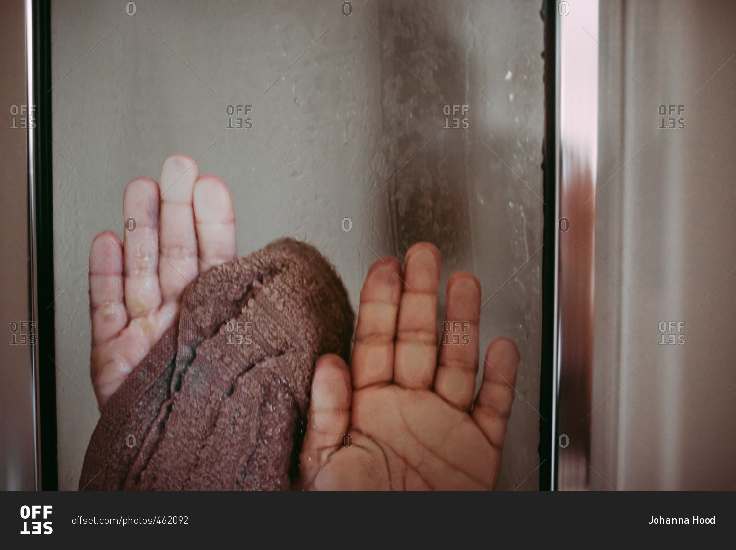 Hands of child with wash cloth pressed up against glass door of the shower