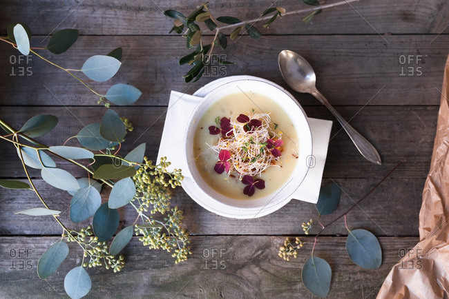 Soup garnished with sprouts and flowers on a rustic table