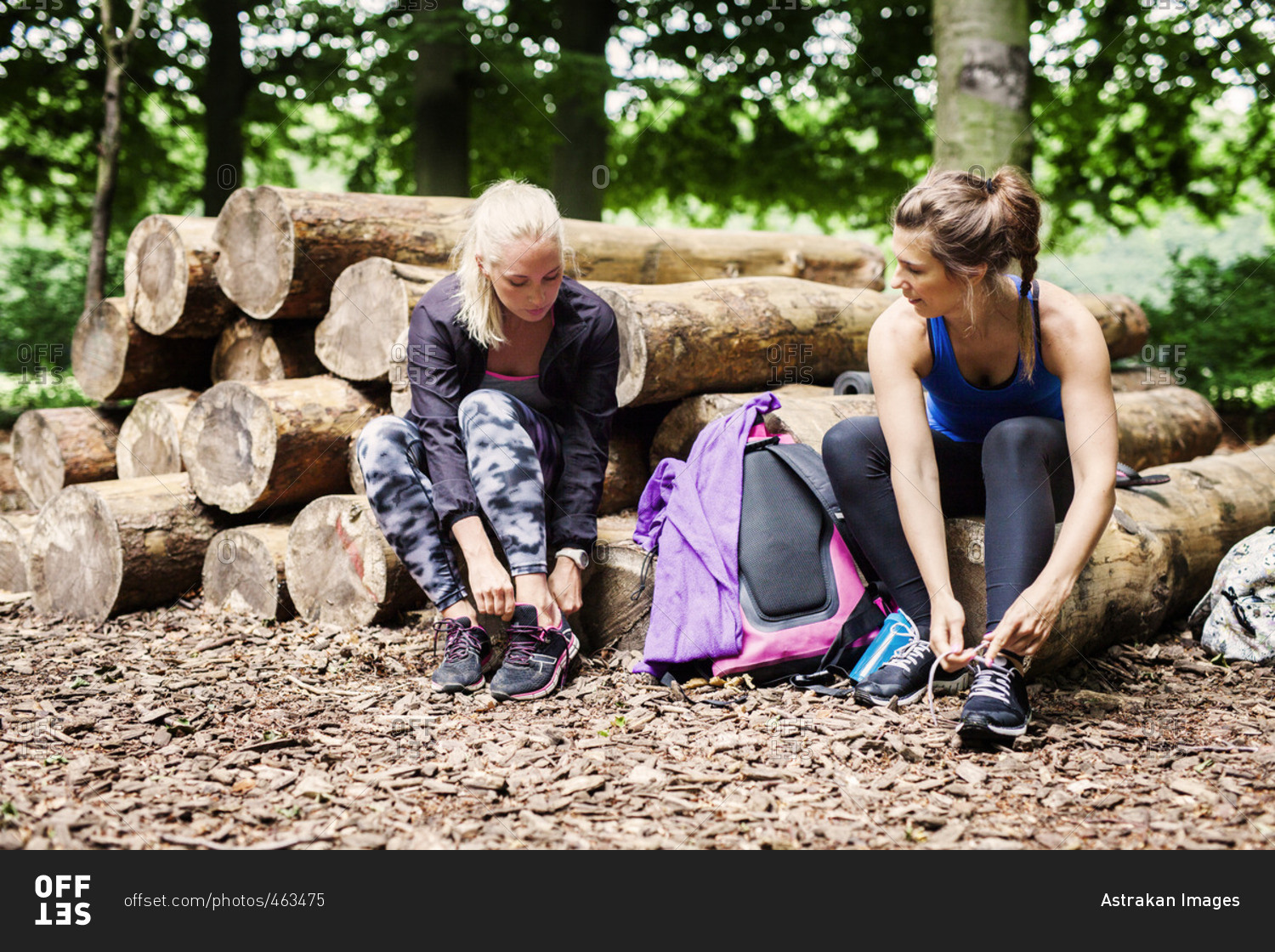 Young women wearing sports shoes while sitting on logs at park