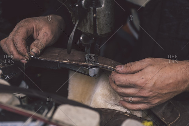 A shoemaker sewing a piece of leather