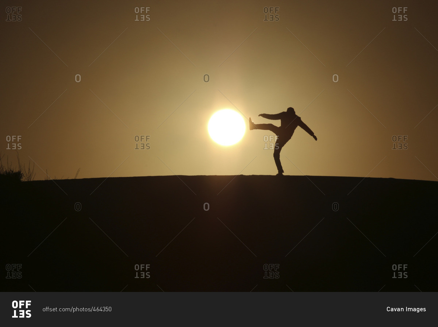 Optical illusion of silhouette man kicking sun during sunset
