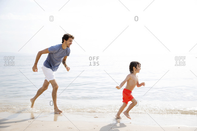 Playful father running behind son at beach