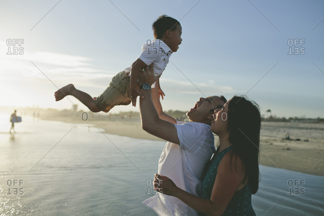 Happy father lifting son while standing with wife at beach