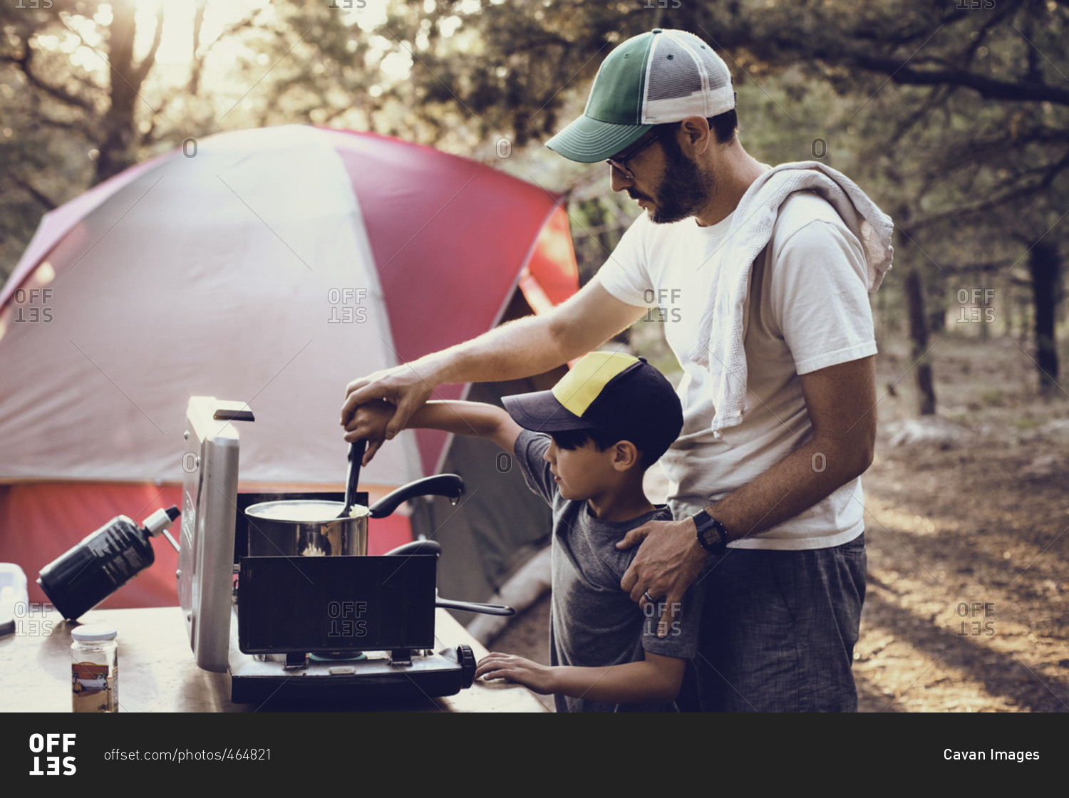 Father and son preparing food on camping stove in forest