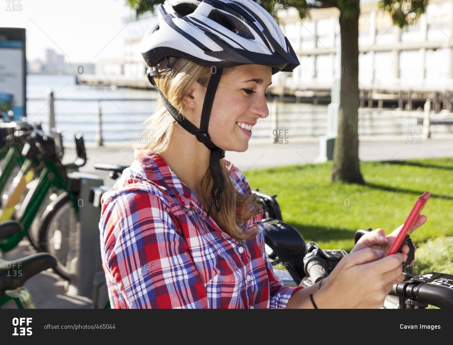 Woman wearing helmet using phone while standing against bicycle rack in city