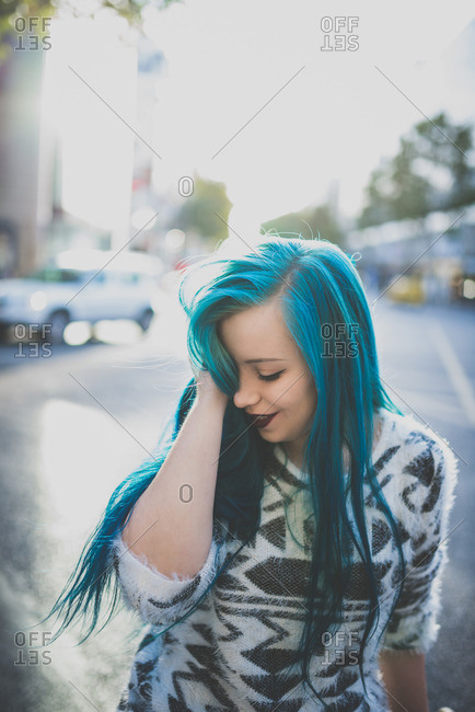 Blue haired punk girl looking down while standing on a city street
