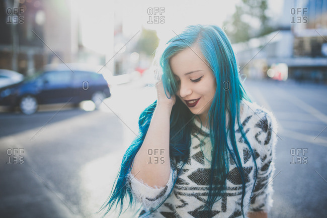 Young girl smoothing her blue straight hair on a city street