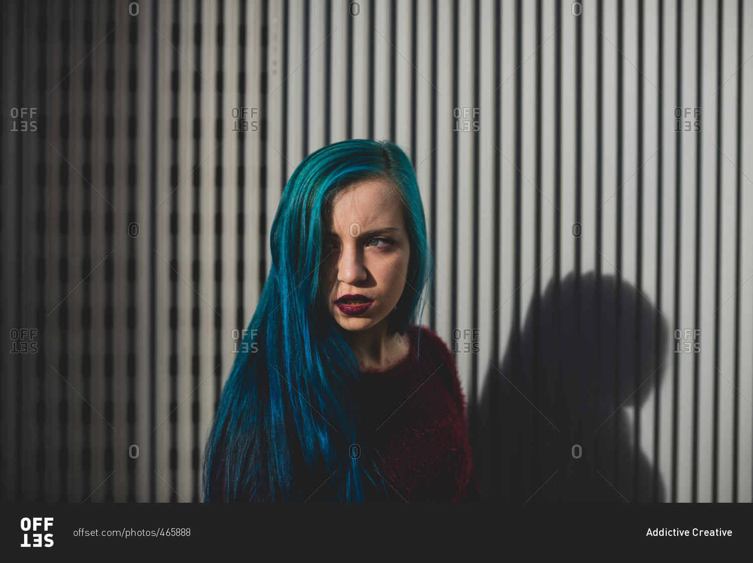 Punk girl with blue hair looking away against striped background