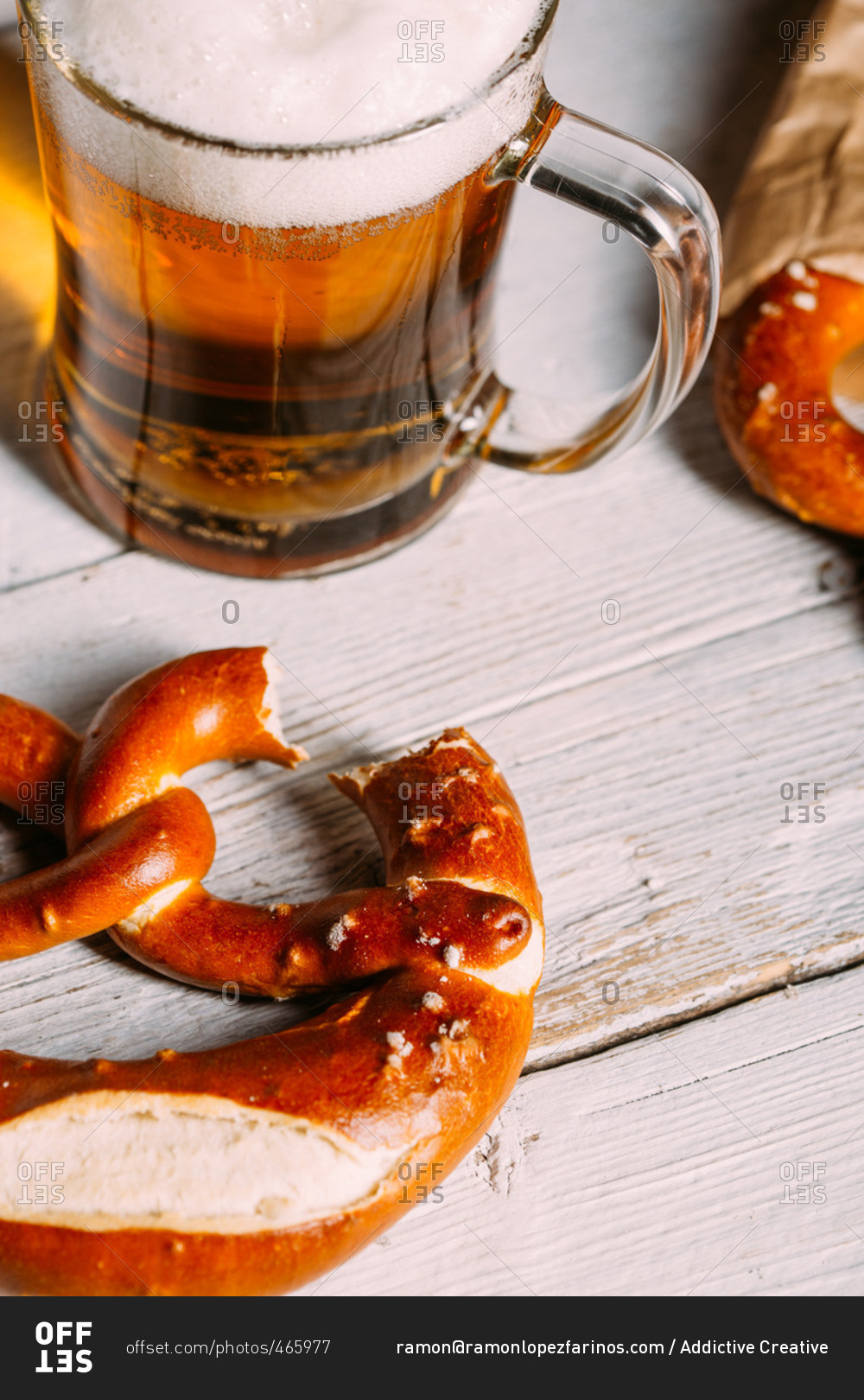 Glass of a beer and pretzel missing a bite on wooden white table