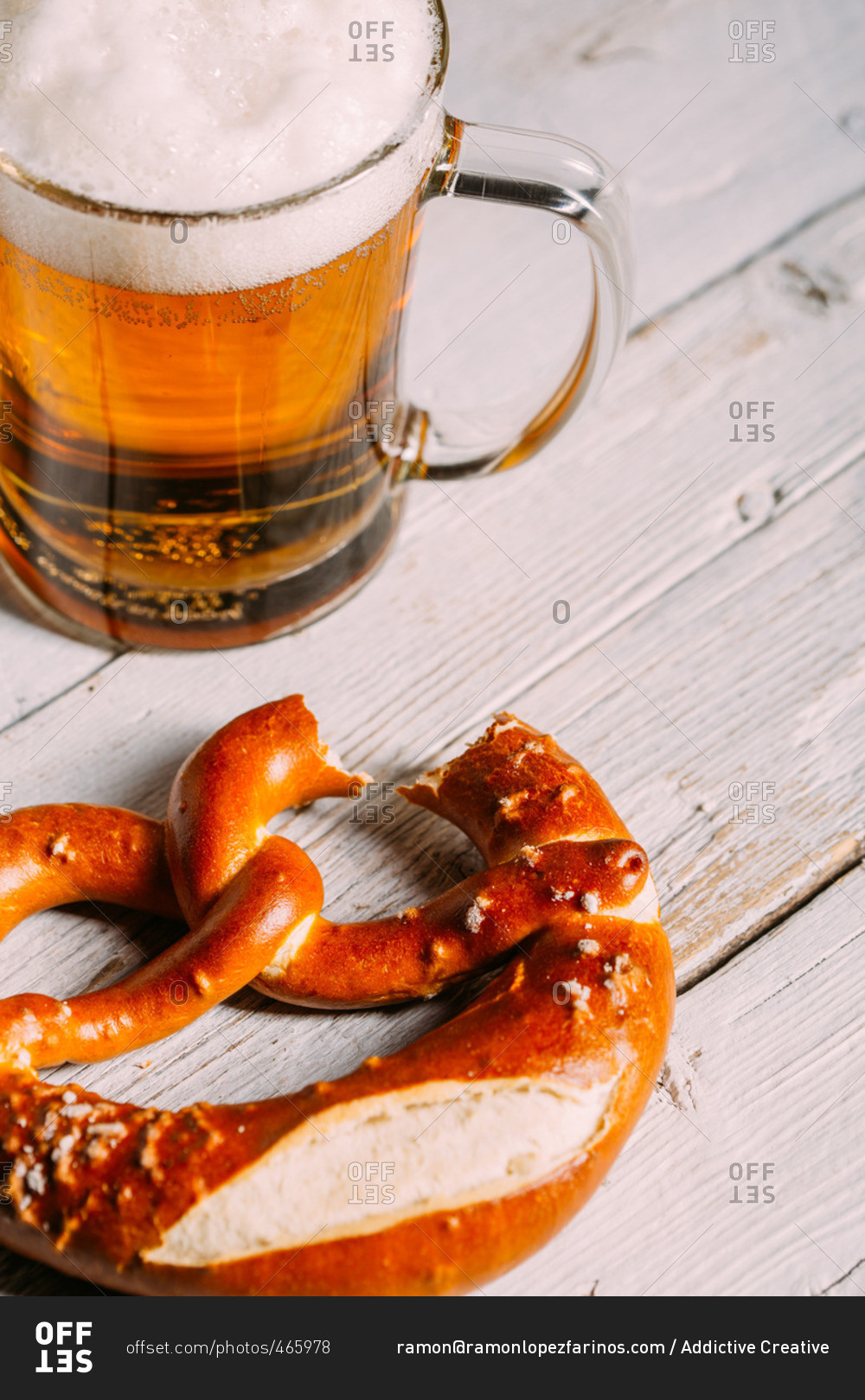 Pretzel missing a bite with a glass of beer on wooden white table