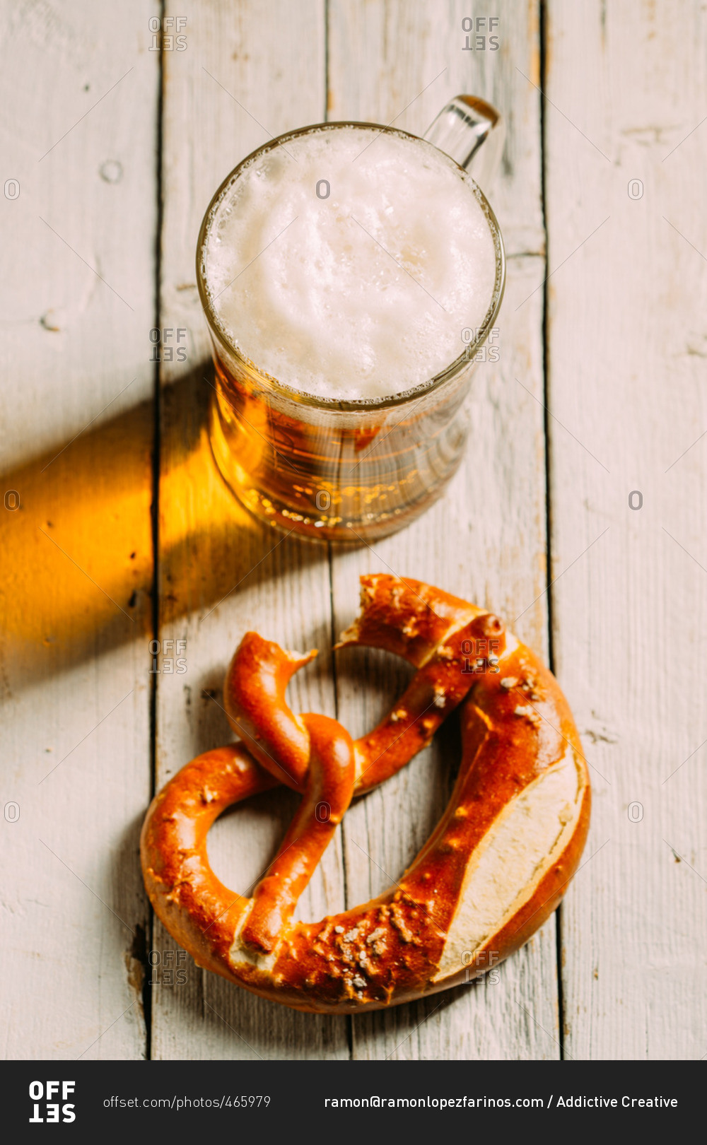 Overhead view of beer and pretzel missing a bite on wooden white table