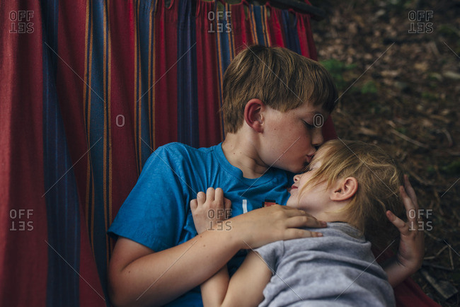Brother Kissing His Sisters Forehead As They Cuddle In A Hammock Stock