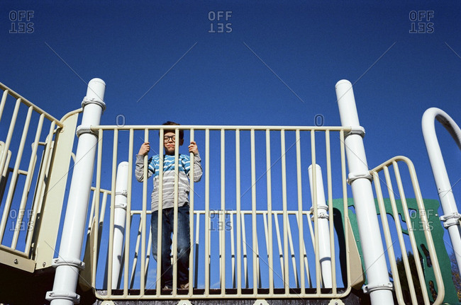 Little boy standing on playground equipment looking through the bars