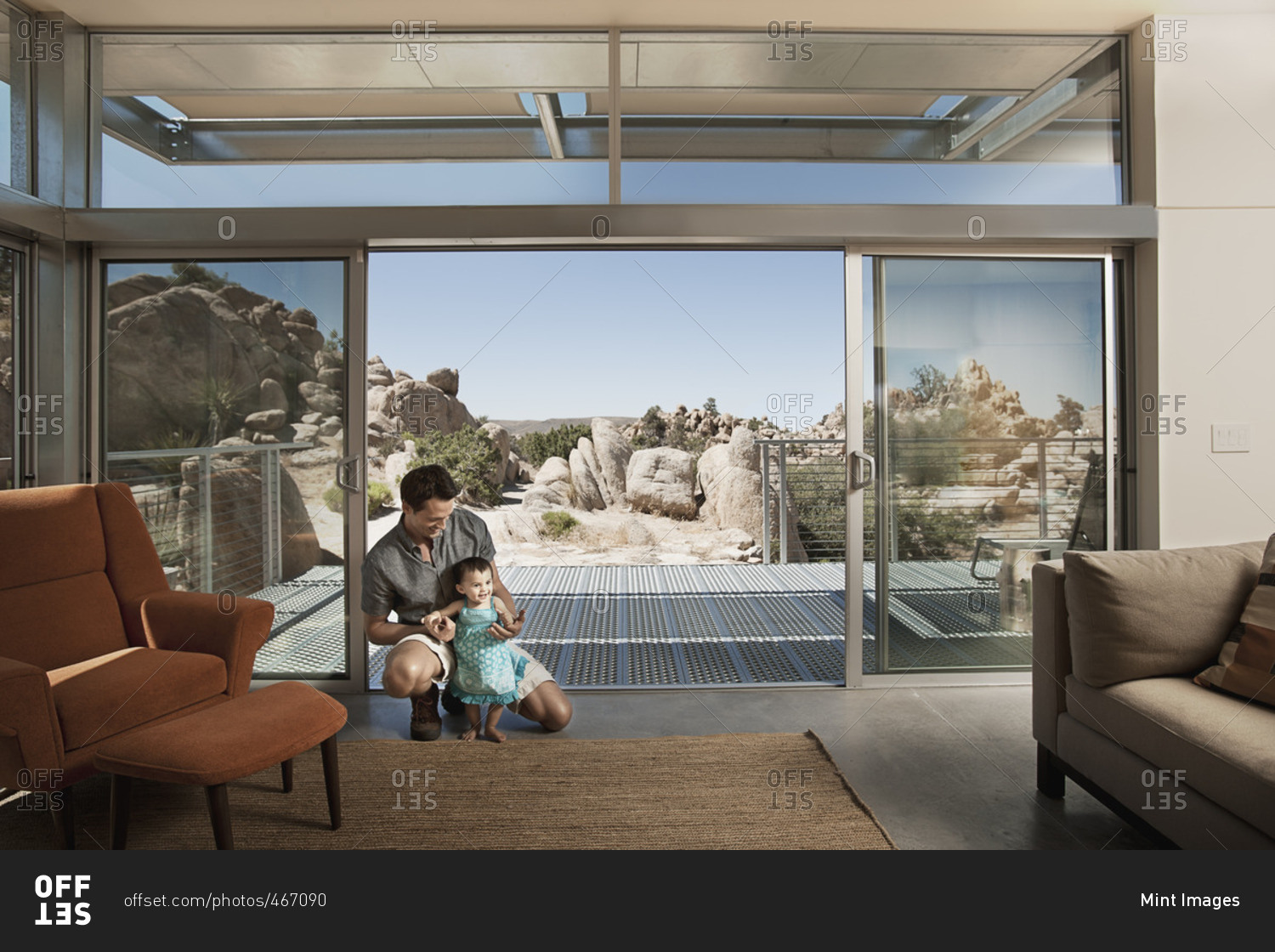 A man and a young child in an ecohouse, a home with large glass walls and view out over the rocky landscape