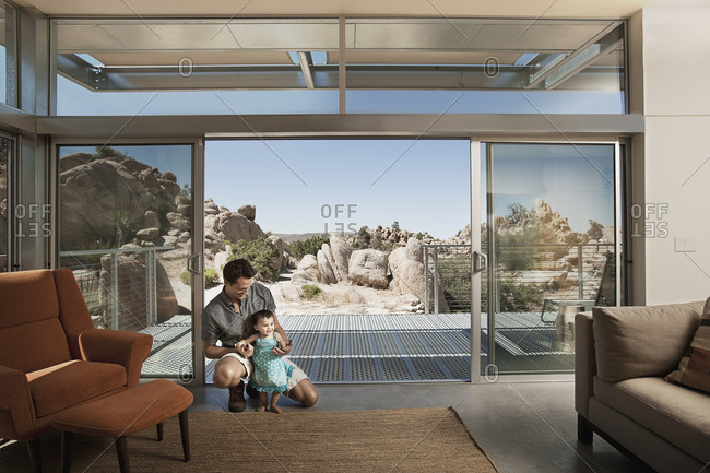 A man and a young child in an ecohouse, a home with large glass walls and view out over the rocky landscape