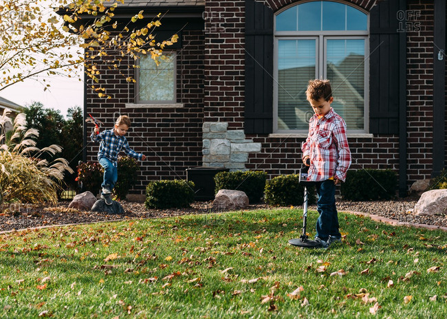 Boy searching his front yard with a metal detector while his brother plays
