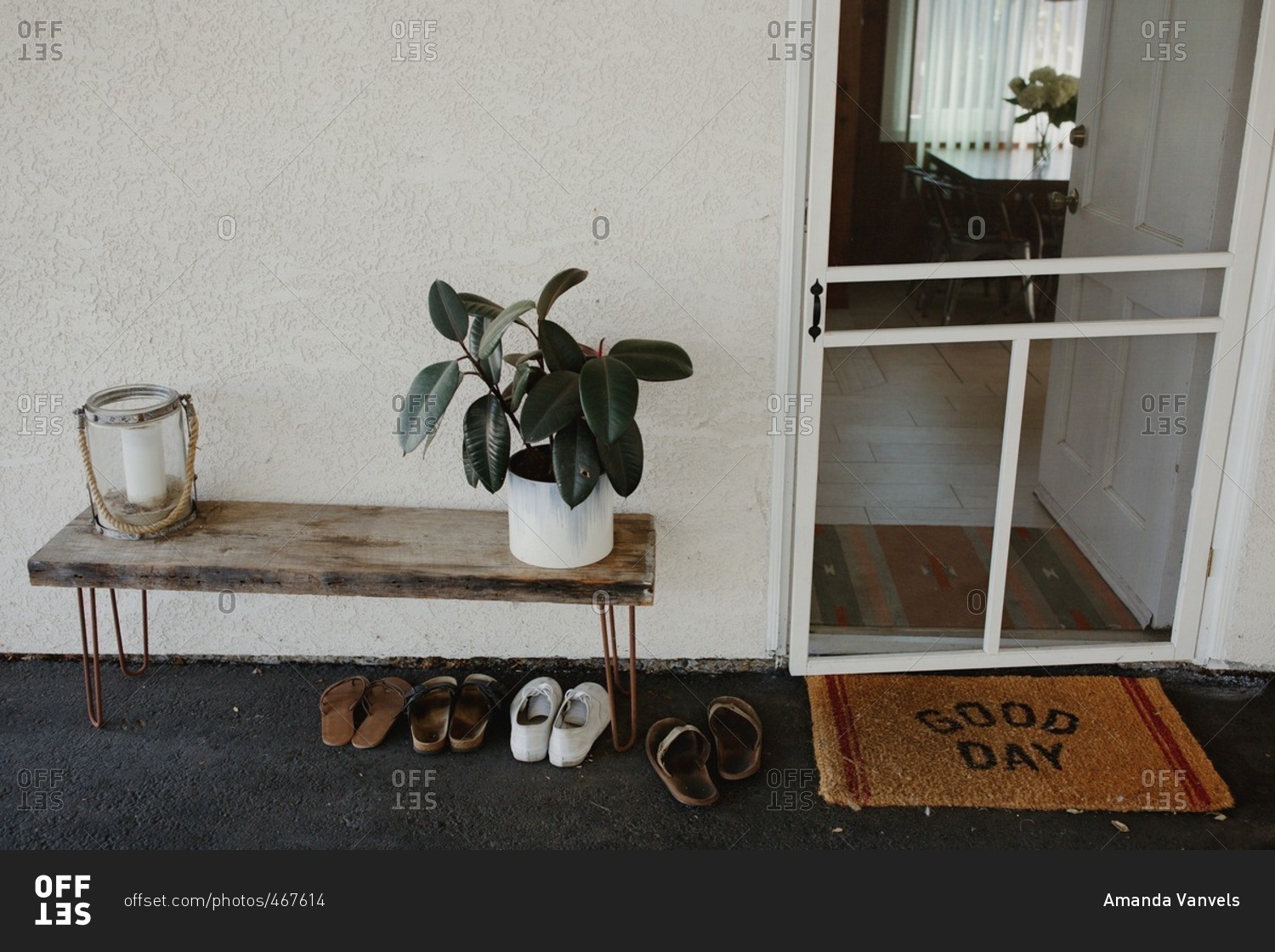 Entrance to house with screen door, welcome mat, and a small table with potted plant