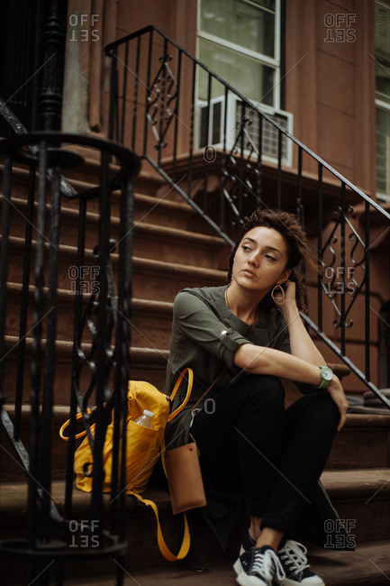 Young woman sitting on steps of Brooklyn brownstone building, New York