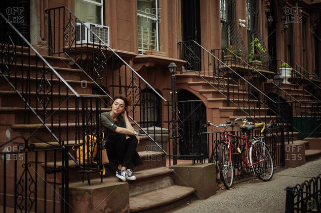 Woman sitting on steps of brownstone building in Brooklyn, New York