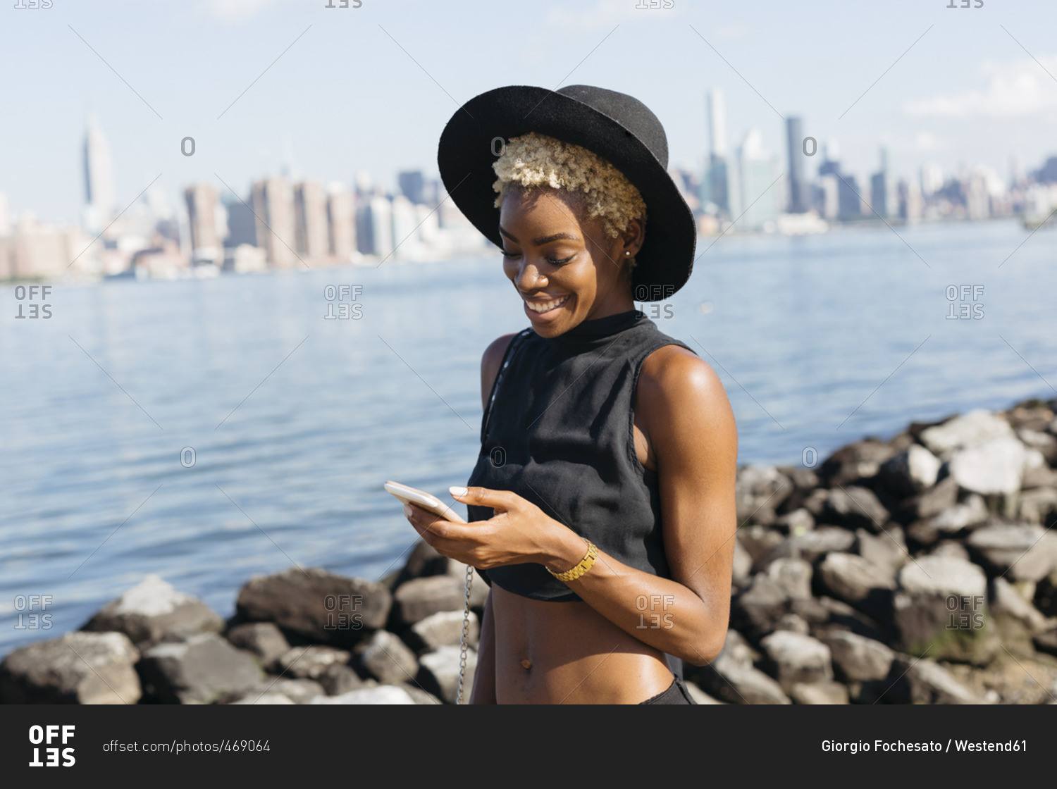 USA- New York City- Brooklyn- smiling young woman at East River looking on cell phone