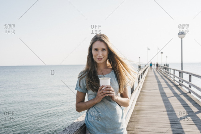 Portrait of happy young woman with coffee to go on jetty