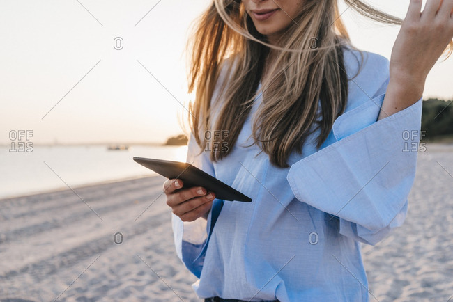 Young woman using tablet on the beach- partial view