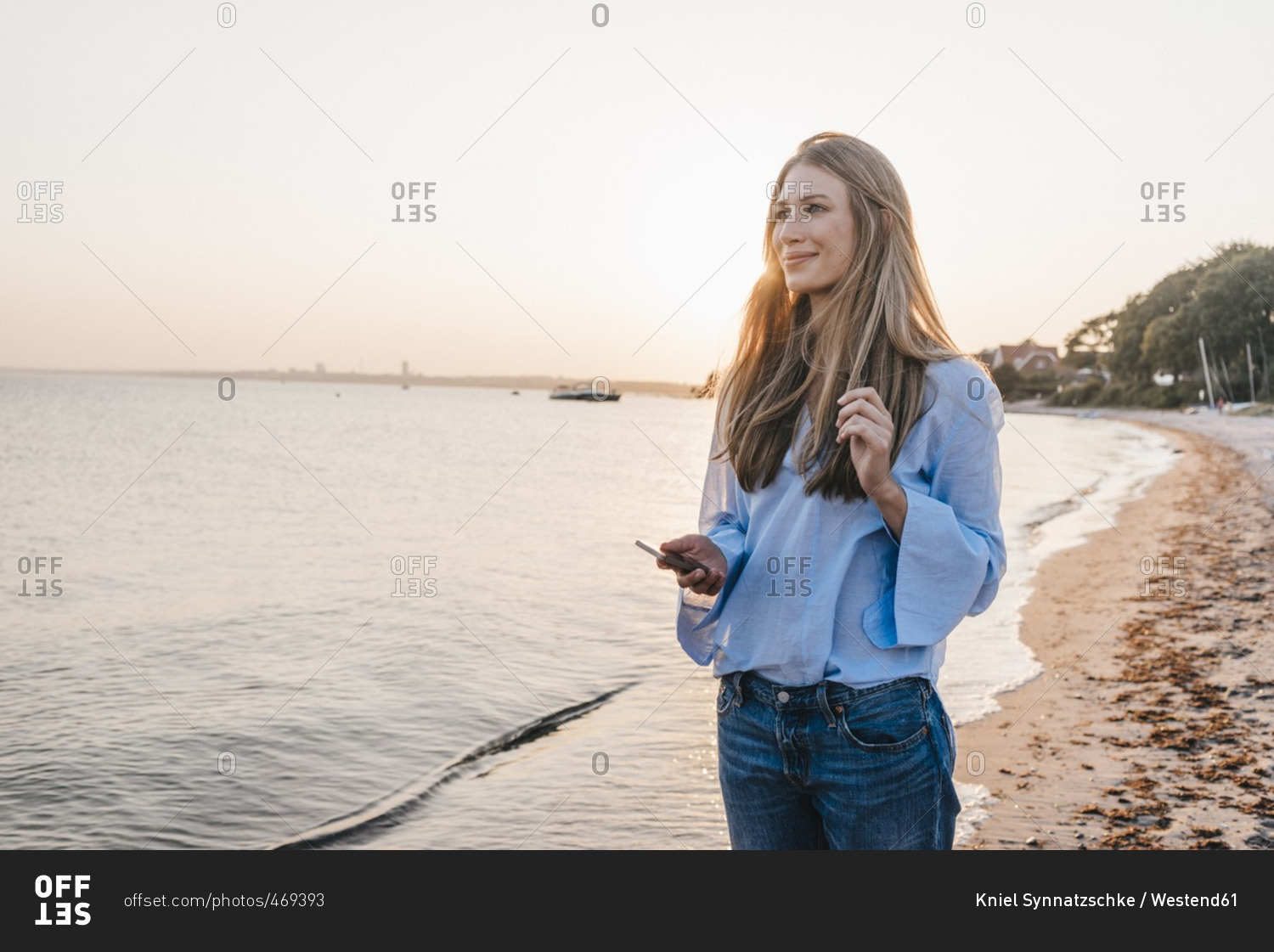 Smiling young woman with smartphone standing on the beach