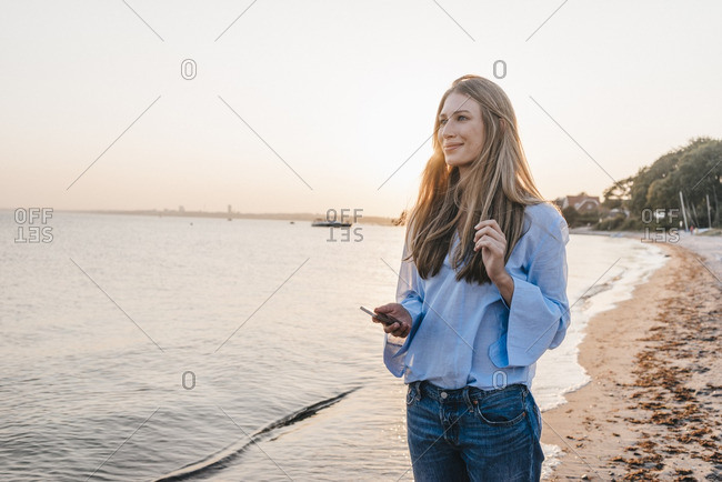 Smiling young woman with smartphone standing on the beach