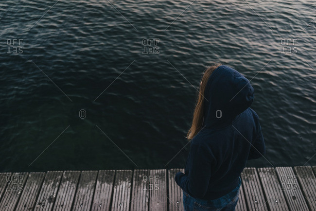 Back view of woman wearing hooded jacket standing in front of the sea