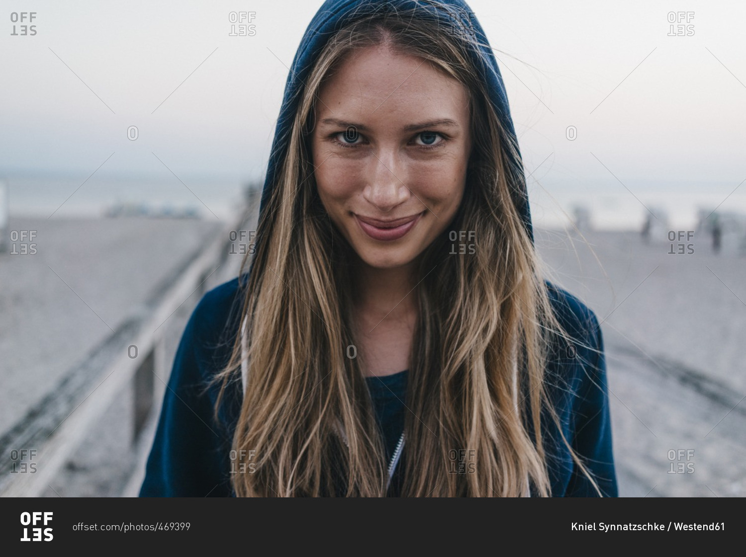 Portrait of smiling young woman wearing hooded jacket standing on jetty stock photo OFFSET