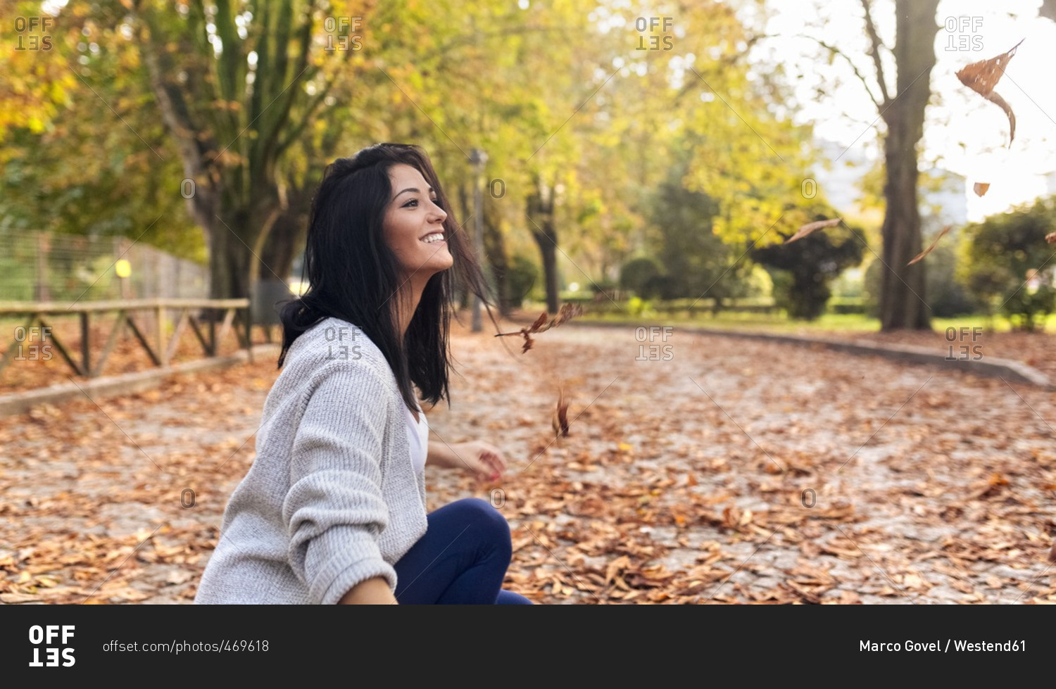 Happy young woman playing with leaves in a park in autumn