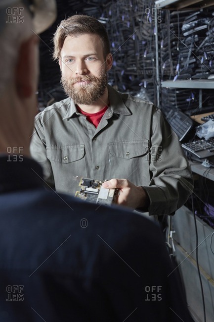 Worker in computer recycling plant giving colleague a component part