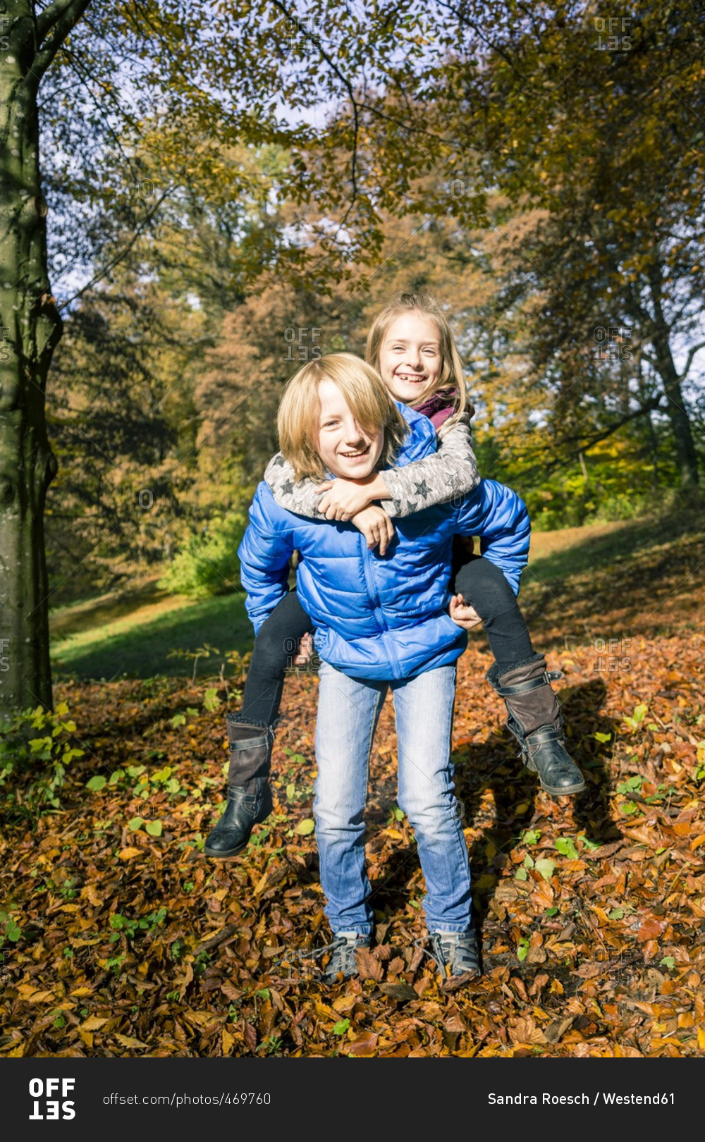 Portrait of boy giving his sister a piggy back ride in autumn