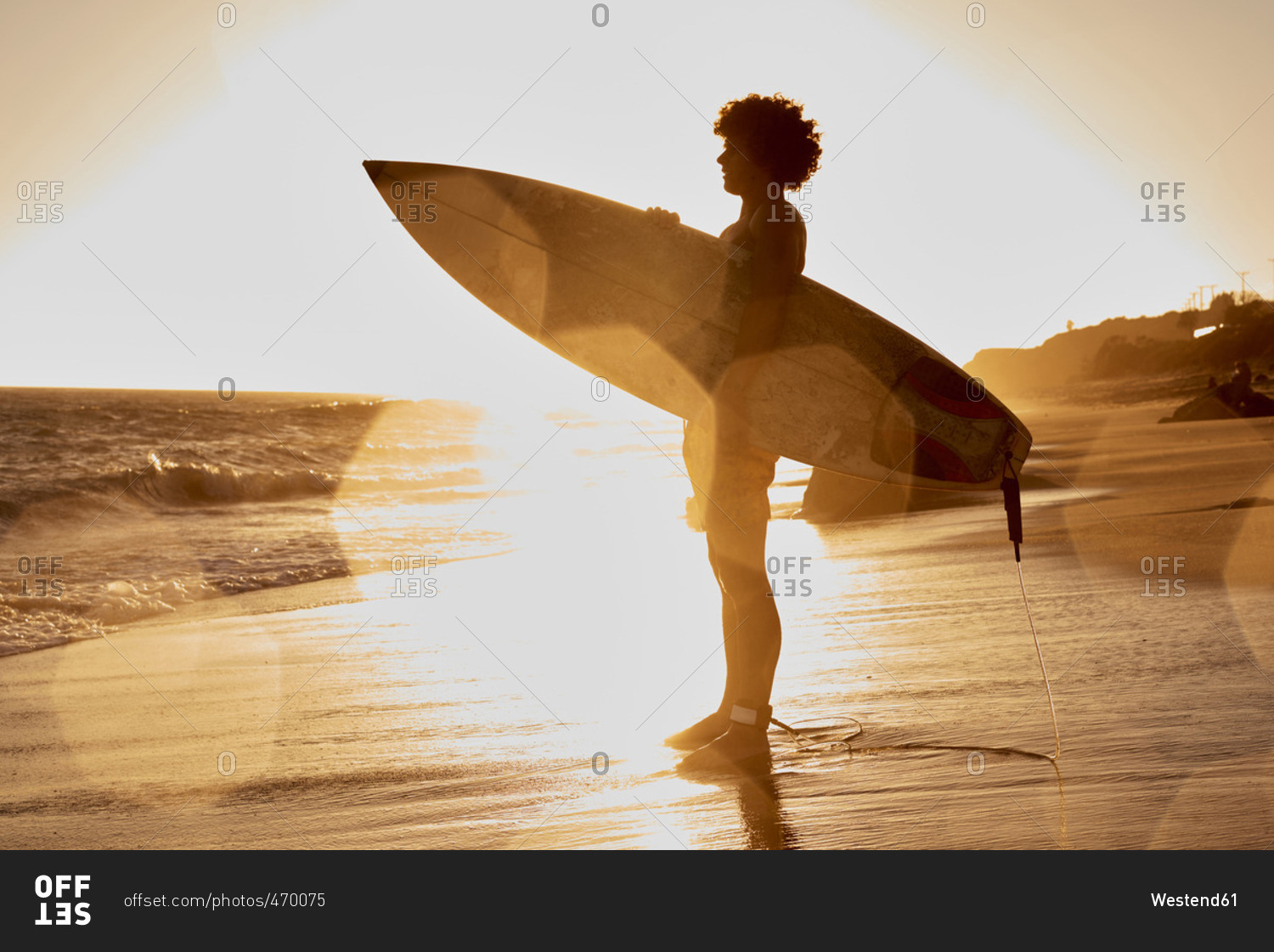 Young man holding surfboard on the beach at sunset