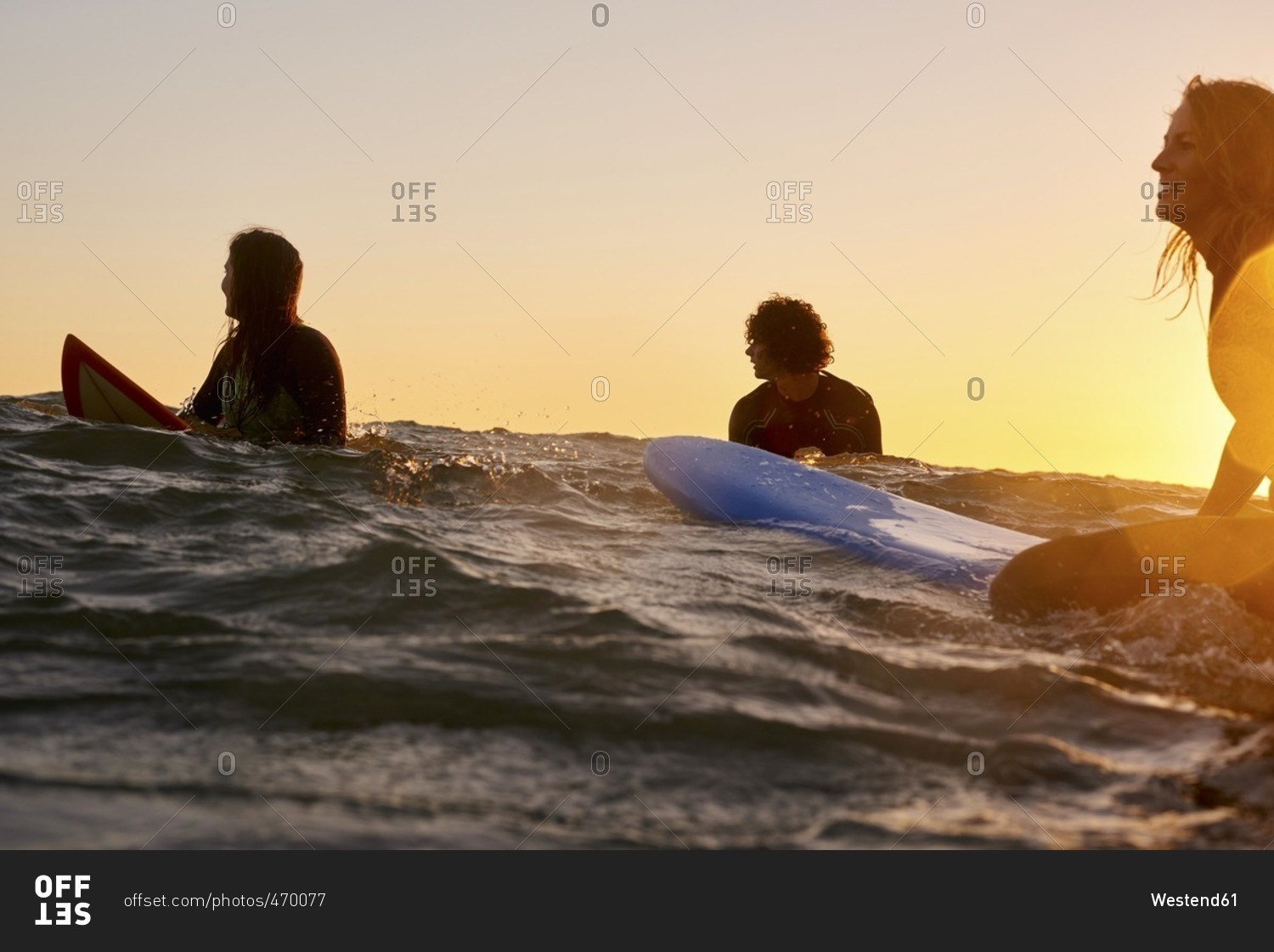 Three surfers in the sea at sunset