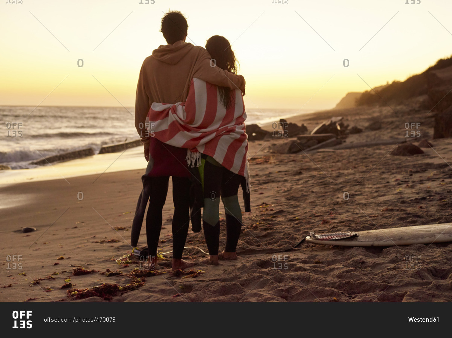 Couple embracing on the beach at sunset next to surfboard